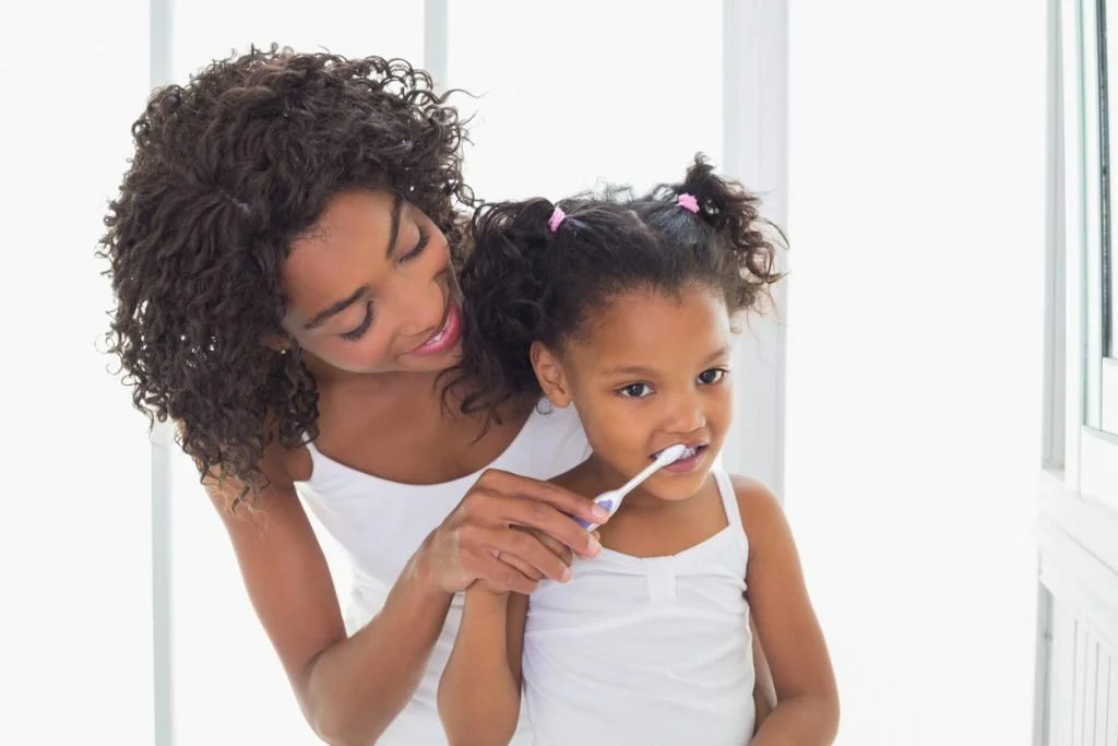 Pretty mother helping her daughter brush her teeth